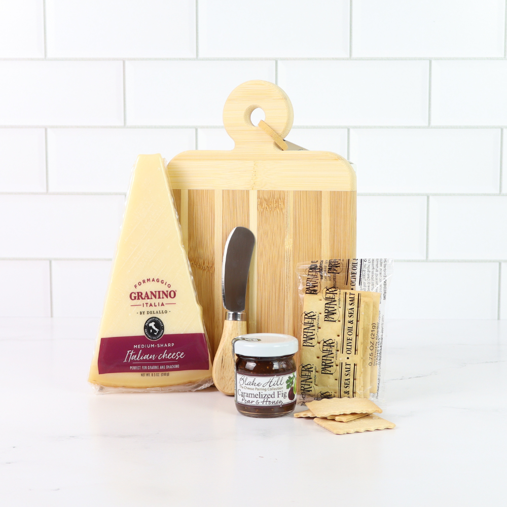 Artisan cheese board gift set with Italian cheese wedge, fig pear honey spread, crackers and bamboo serving board on white marble background