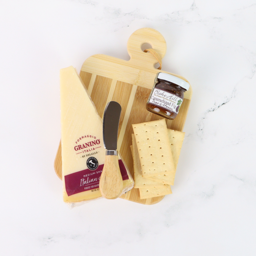 Wooden cutting board with cheese, a knife, and a jar of jam on a white surface