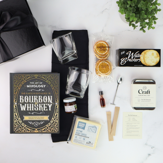 Bourbon whiskey-themed gift set with books, glasses, and snacks on a white surface.